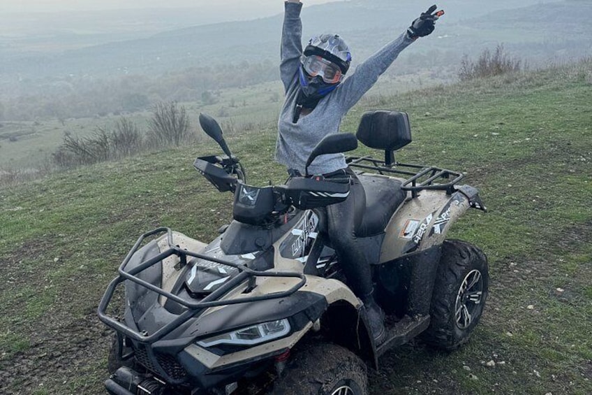 A person on a quad bike in a grassy field with a hilly landscape in the background. 4
