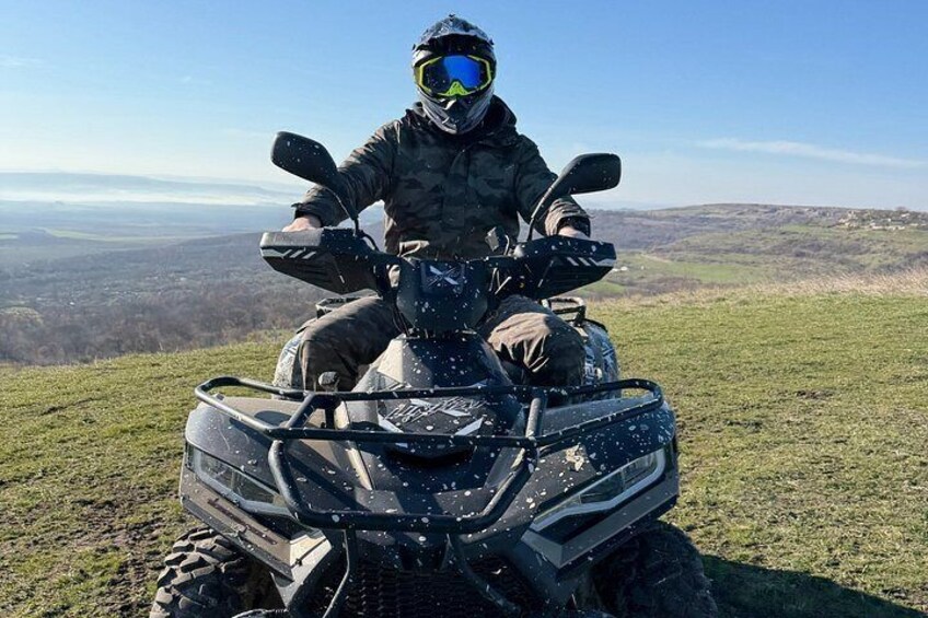 A person on an ATV on a grassy hill with a view of a valley. 3