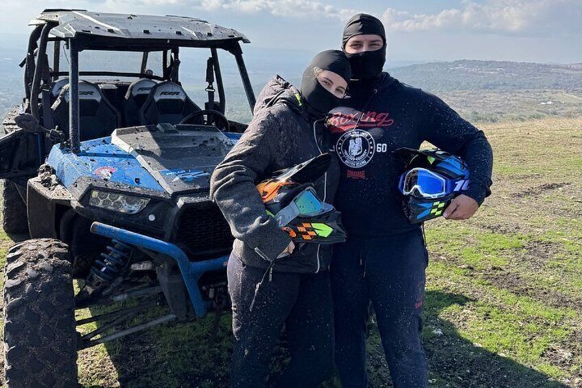 A person standing next to a blue ATV on a grassy hill with a helmet and a jacket. 5