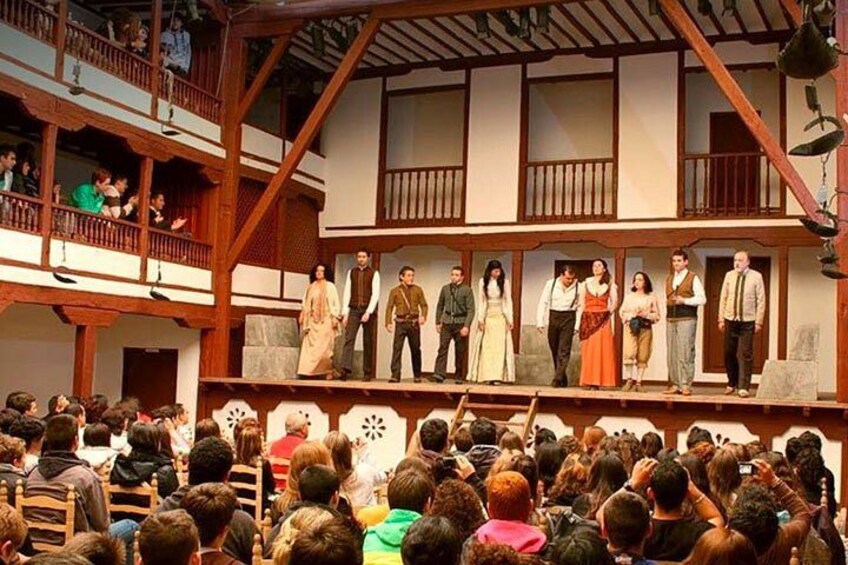 A group of people on a stage in a wooden building with a balcony, surrounded by an audience. 3