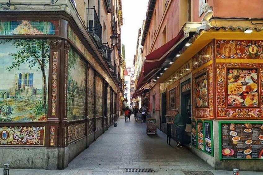A narrow street with colorful murals and restaurant signs. 1