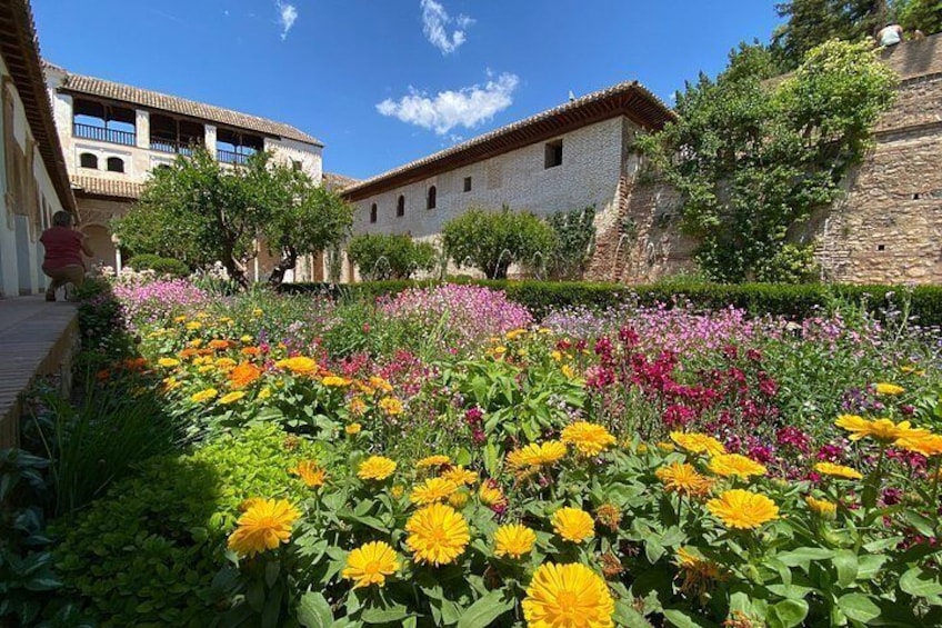 A courtyard with colorful flowers, stone buildings, and a clear blue sky. 5