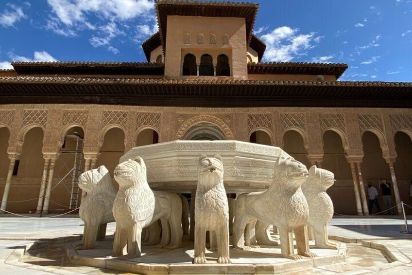 Ein Innenhof mit einem Brunnen, der von vier Löwenstatuen geschmückt wird, und einem Gebäude mit Bögen im Hintergrund. 1