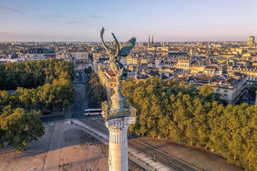 A statue with wings, surrounded by trees and buildings, with a train track in the foreground. 2