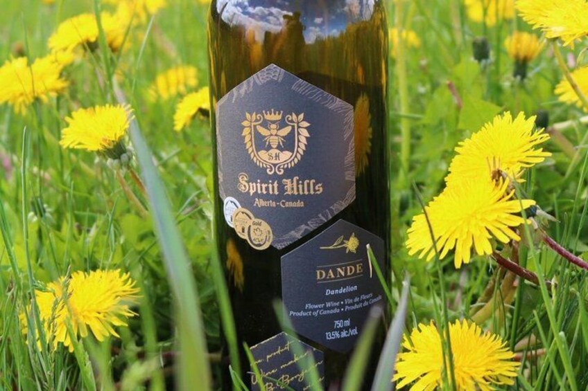 Una botella de vino Dande de Spirit Hills con etiqueta, rodeada de dientes de león amarillos. 2