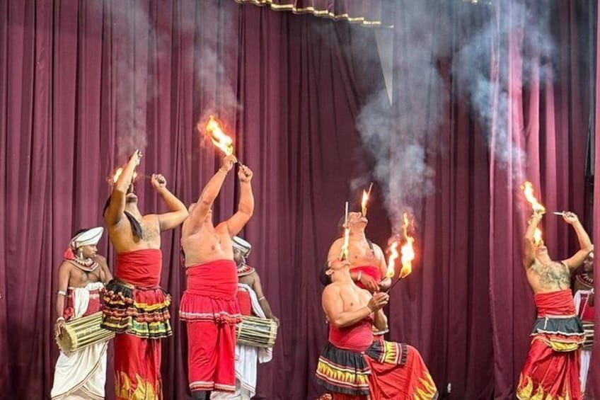 Eine Gruppe von Darstellern in traditioneller Kleidung mit Fackeln tritt vor einer burgunderfarbenen Bühne auf. 4