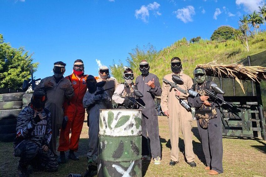 En gruppe mennesker i paintballudstyr står udendørs omgivet af træer under en klar himmel. 1