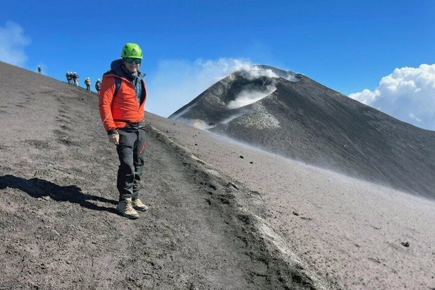A person standing on a volcanic slope with a mountain in the background. 1