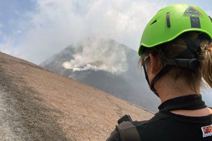 A person wearing a green helmet and black clothing, standing on a rocky terrain with a mountain in the background. 4