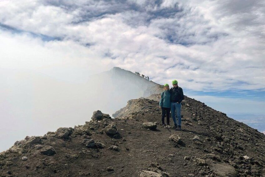 Two people standing on a rocky mountain peak with a cloud-covered sky in the background. 2