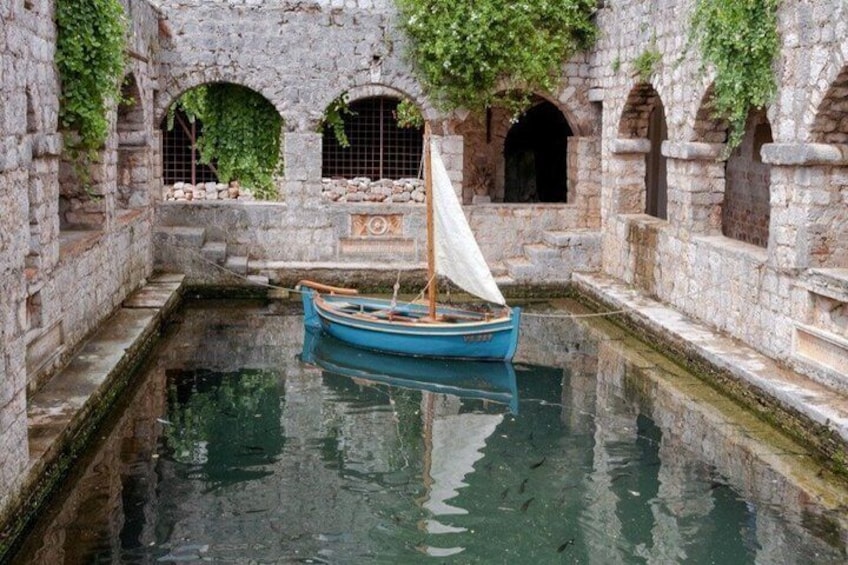 A boat in a stone-lined canal with arched windows and greenery. 1