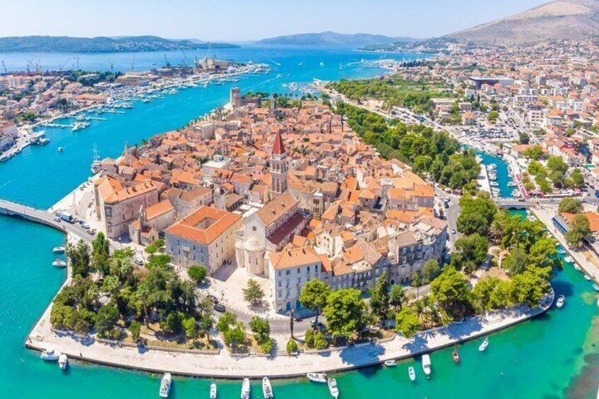 Una città costiera con una chiesa importante, un porto con barche e montagne sullo sfondo. 1
