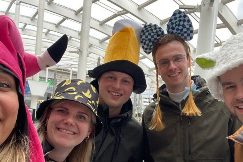 A group of people in a covered outdoor area with a glass roof, wearing various hats and costumes. 2