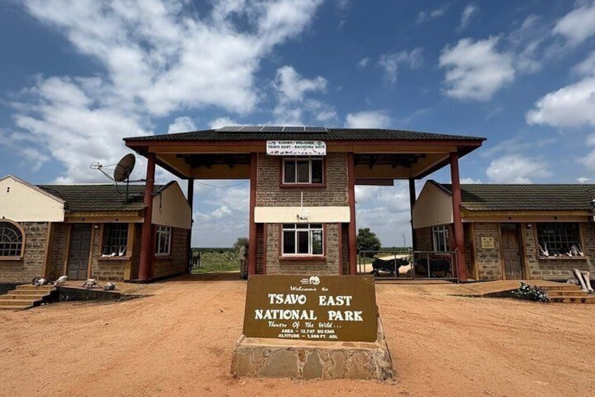 Entrée du parc national de Tsavo-Est, avec un panneau indicateur, des bâtiments et un ciel dégagé. 4