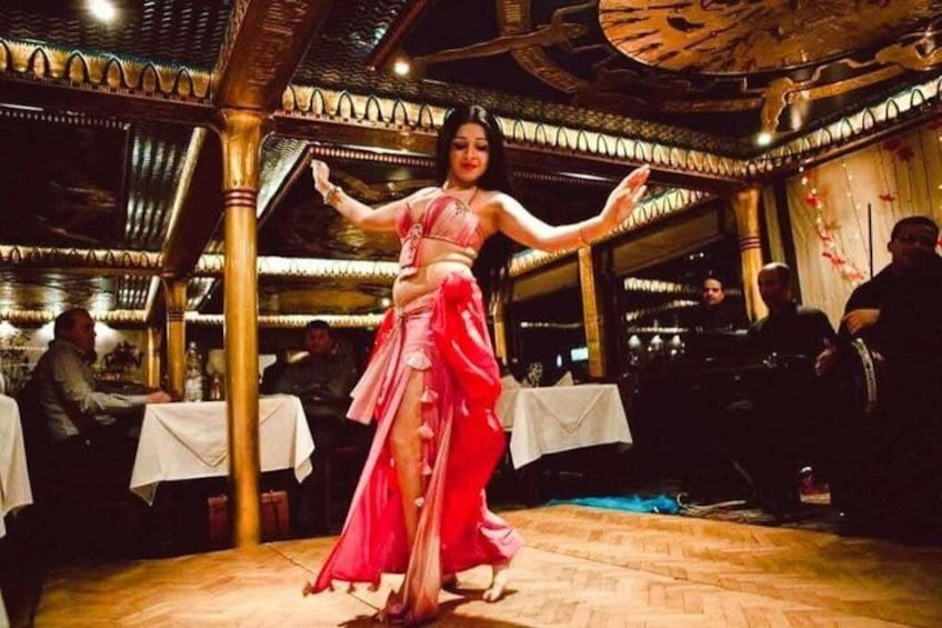 Une femme vêtue d’une robe rose danse dans un restaurant dont le sol est en bois et dont le plafond est orné de d écorations élaborées. 1