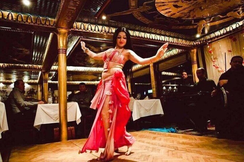 A woman in a pink dress performing a dance in a restaurant with ornate ceiling and wooden flooring. 1