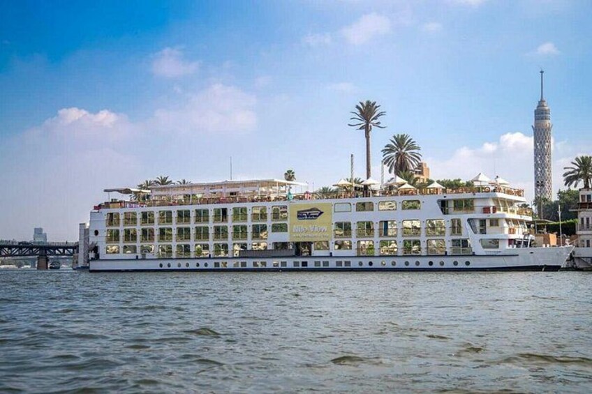 Un bateau de croisière fluviale doté de plusieurs ponts, de palmiers et d’une haute tour en arrière-plan. 2