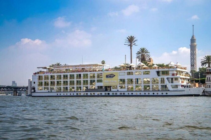 A large river cruise ship with multiple decks, a bridge, and a tall tower in the background. 2