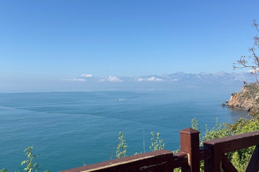 Vista sulla costa con ringhiera in legno, mare calmo e montagne sullo sfondo. 2
