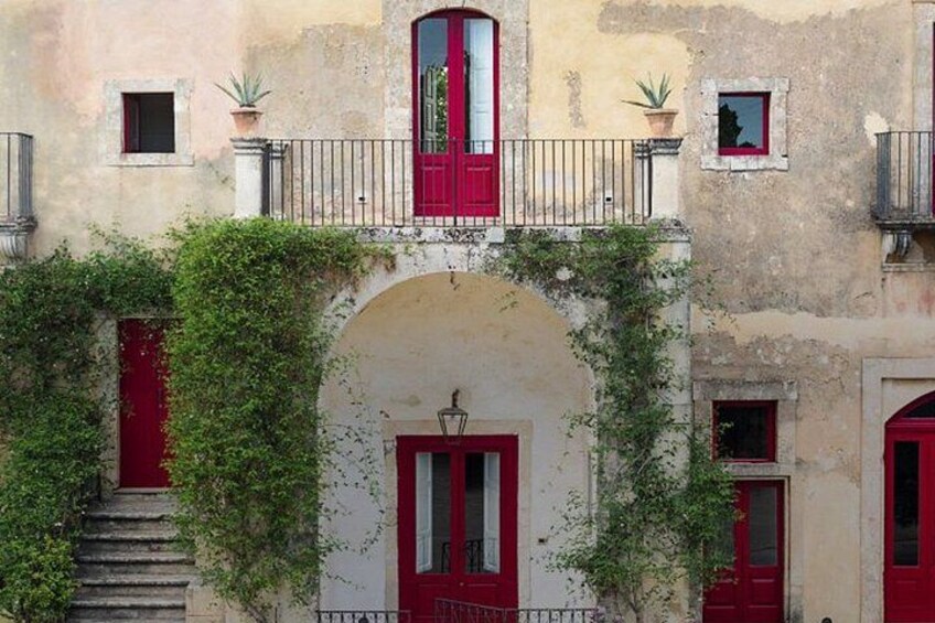A building with red doors and windows, an arched entrance, and a balcony with potted plants. 4