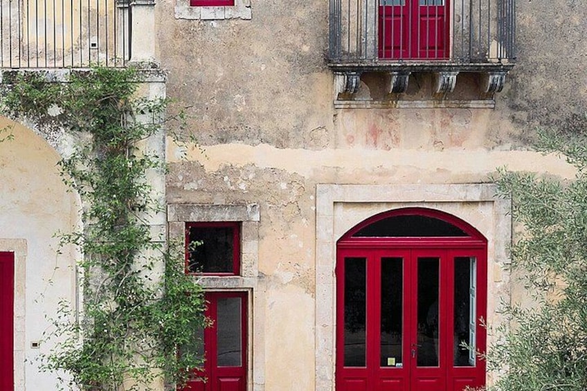A building with red doors and windows, a balcony with a railing, and some greenery. 5