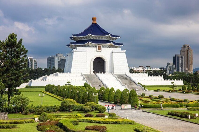 A traditional white building with a blue roof, surrounded by well-manicured gardens and a cityscape in the background. 1