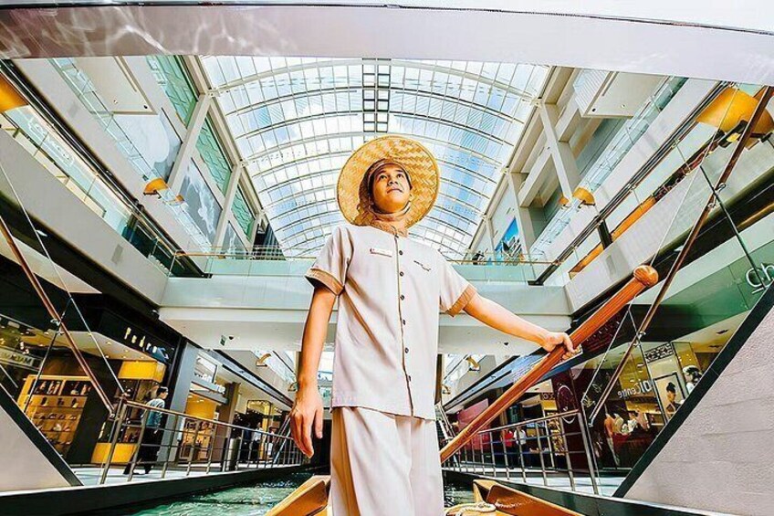 A person in a boat in a modern indoor setting with glass ceilings and escalators. 5