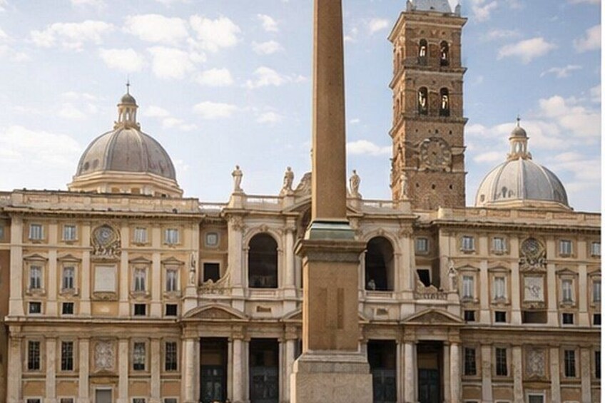 A historic building with domed roofs, a tall clock tower, and a central column. 5