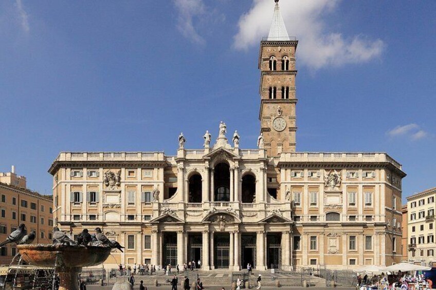 A large historic building with a prominent clock tower, a fountain, and a busy public square. 4