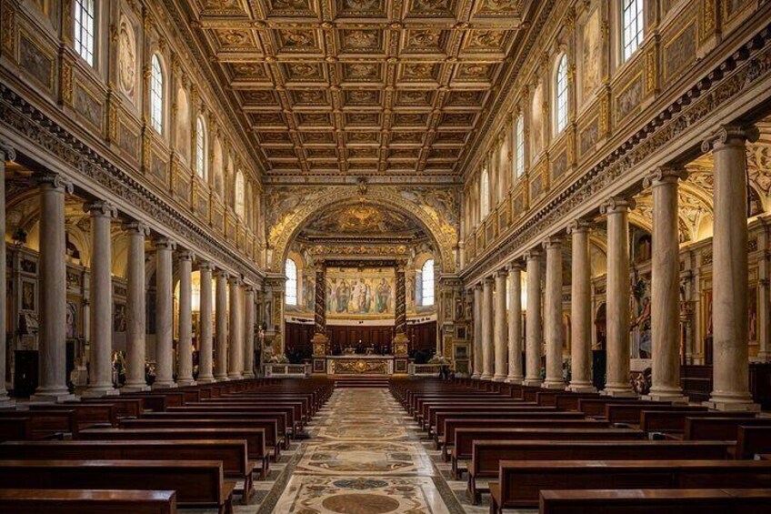A grand hall with rows of wooden pews, a high ornate ceiling, and a central altar. 2
