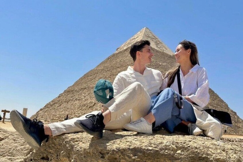 Due persone sedute su una roccia, con una piramide sullo sfondo. 1