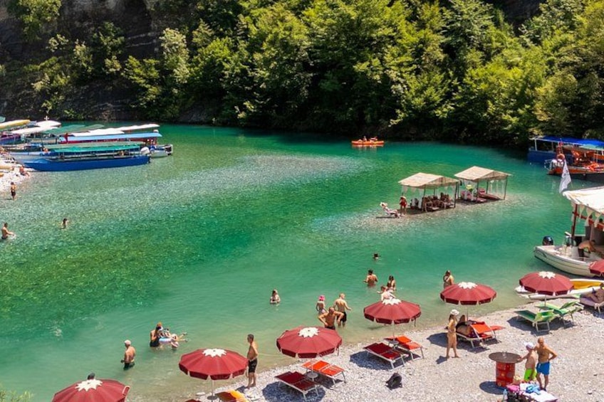 A beach with clear turquoise water, people swimming and sunbathing, and boats docked nearby. 1