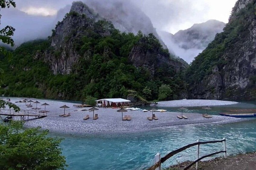 A river with a pebbled beach, surrounded by lush greenery and rocky cliffs. 2