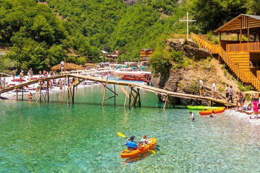 A wooden bridge over clear water, people on the bridge, and a kayak in the water. 4
