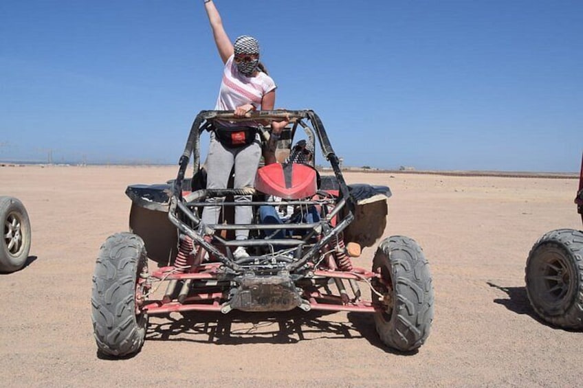 A desert landscape with a red off-road vehicle and a person raising their arm. 2