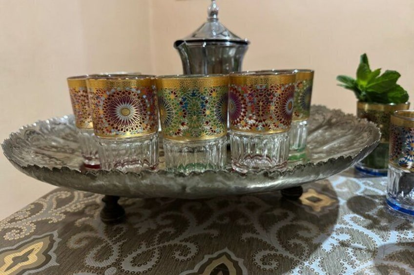 Una bandeja con cuatro vasos de vidrio ornamentados y una jarrón de plata sobre un mantel estampado. 2