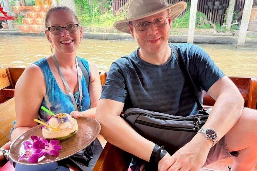 Two people sitting on a boat, one holding a plate with a dessert and a drink. 5