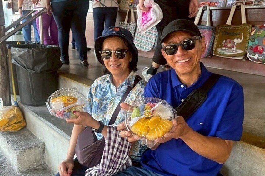 Two people holding food items, sitting on steps with a trash bin and a bag in the background. 4