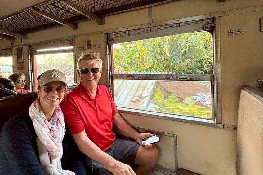 Two people seated on a train, with a window view of greenery outside. 2