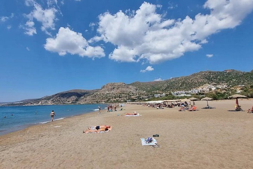 Een strand met mensen die zonnebaden, parasols en een bergachtige achtergrond. 2