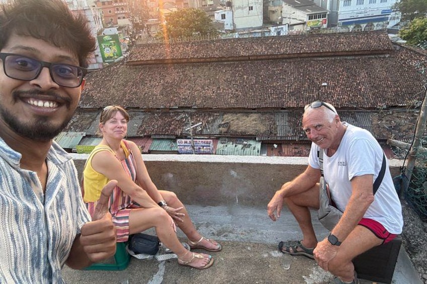 Drie personen zitten op een dak, met een traditioneel pannendak op de achtergrond. 1