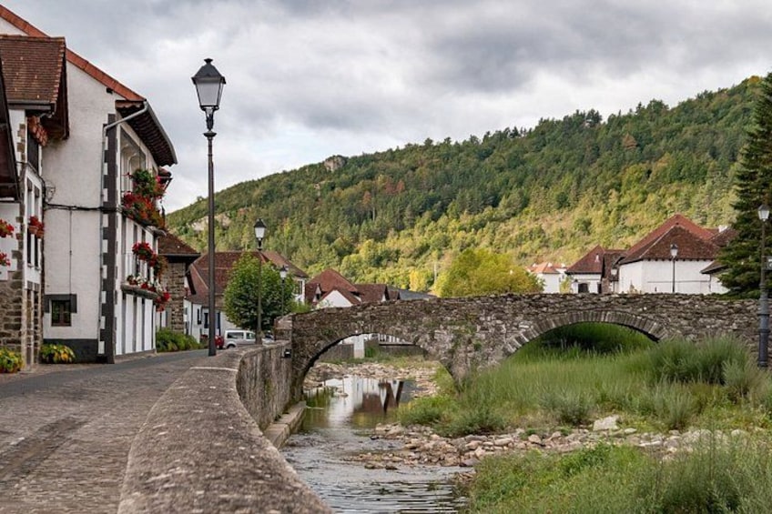 A stone bridge over a river, surrounded by buildings with red-tiled roofs, and a forested hillside in the background. 2