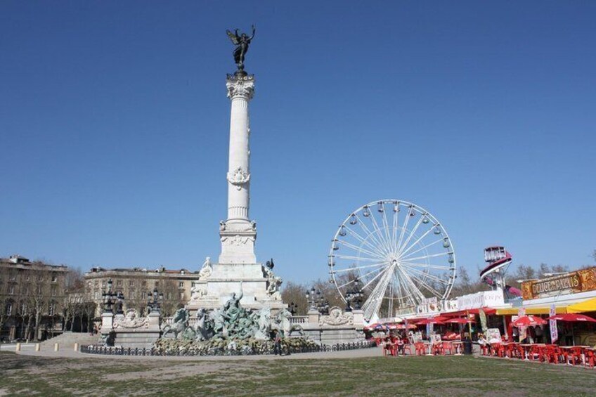 A tall monument with a statue on top, a large Ferris wheel, and a carousel in the background. 5