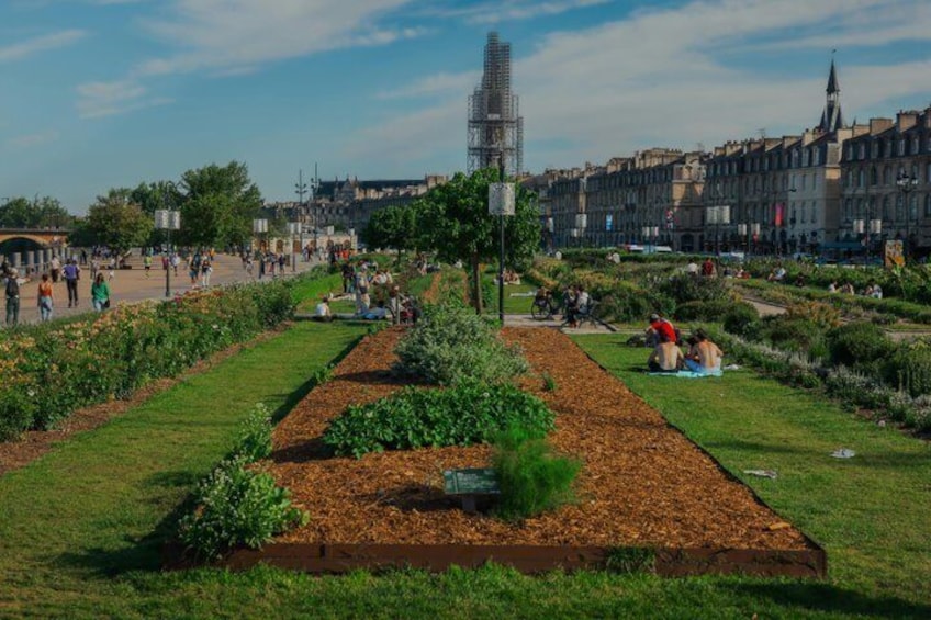 A public square with gardens, people walking, and historic buildings in the background. 3