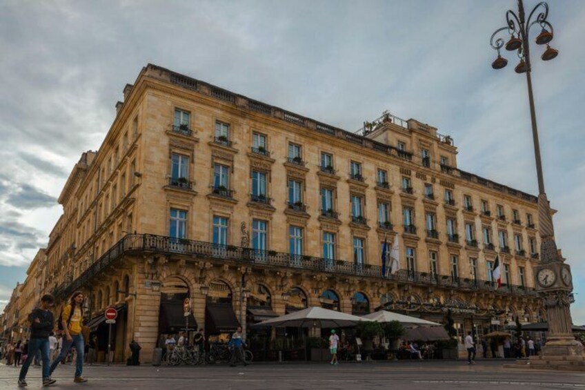 A historic building with a clock tower, ornate balconies, and outdoor seating. 2