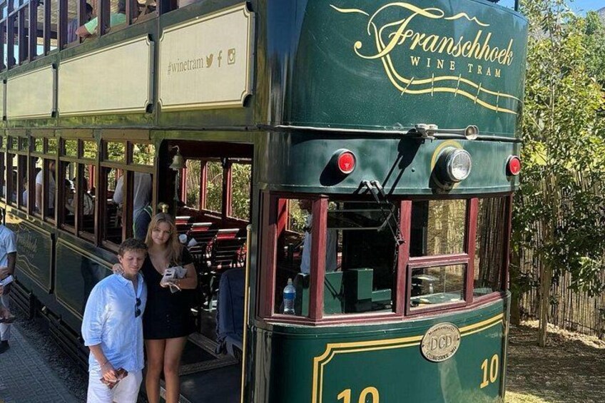 Een klassieke tram met het nummer 10, met de tekst 'Franschhoek Wine Tram', geparkeerd buiten. 1