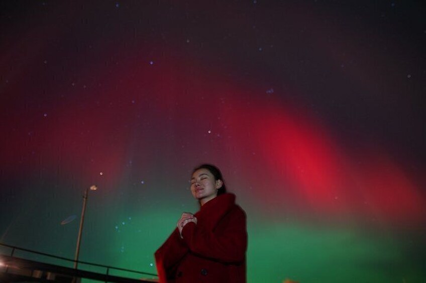 A person in a red coat under a night sky with visible stars and a greenish aurora. 1