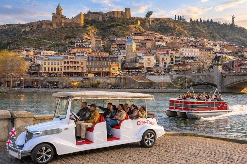 A city tour vehicle on a cobblestone path with a river and historic buildings in the background. 1