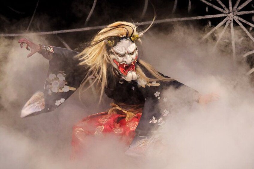 Un artiste vêtu d’un costume traditionnel japonais et portant un masque, dans une pose dynamique, entouré de fumée. 2