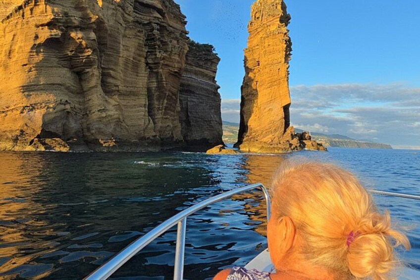 A boat with a person in the foreground, rocky cliffs, and calm water. 5